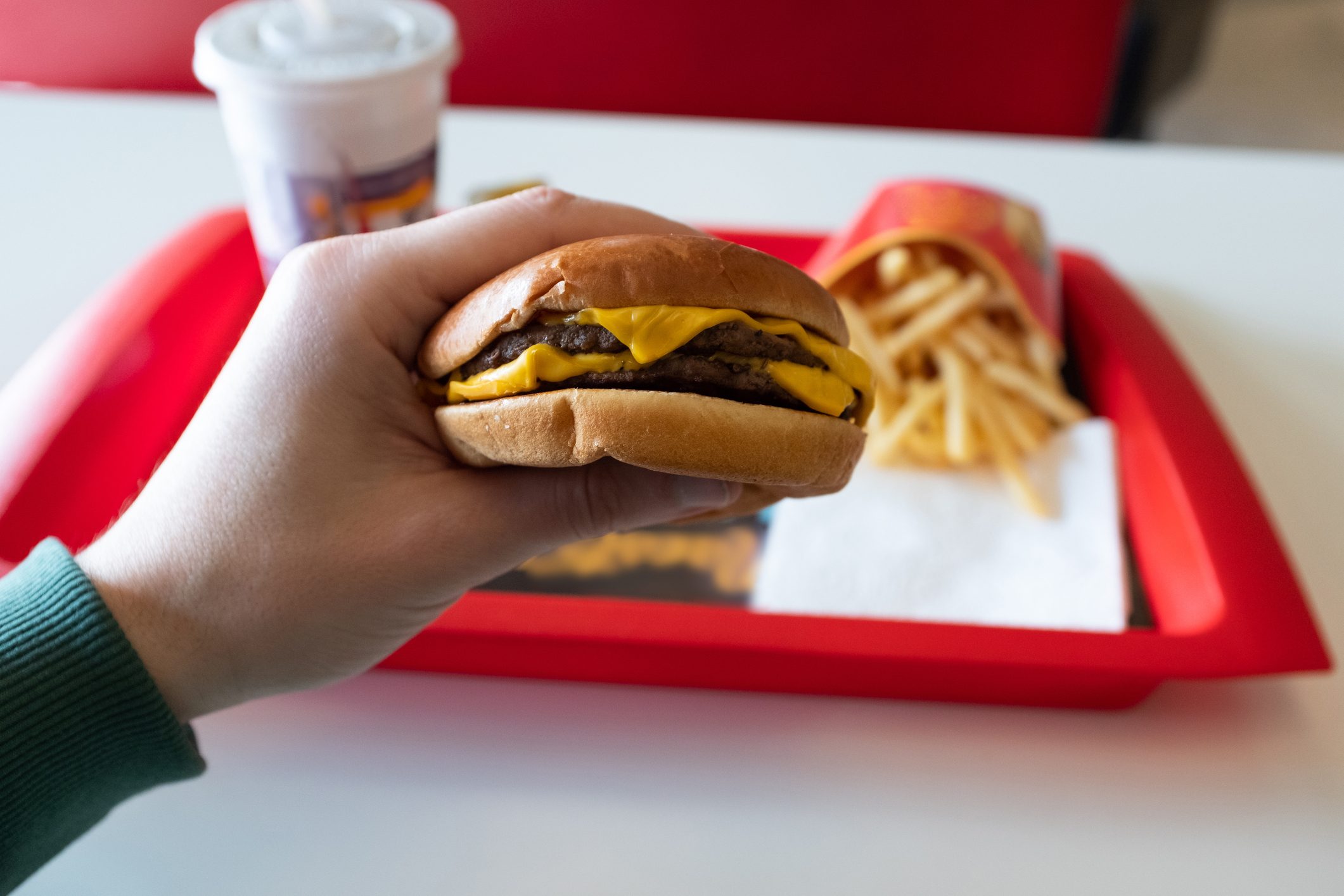 A young man is holding a piece of hamburger in his hands. A guy or a man eats fast food. A hungry skinny guy is eating an appetizing burger. The concept of unhealthy food, diet, overeating, gluttony, dependence on food. Fast food restaurant, snack bar.