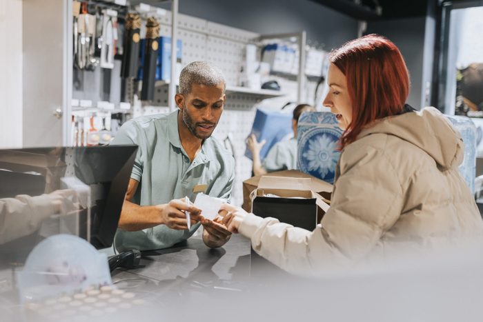 Male retail clerk showing bill to female customer at checkout in electronics store