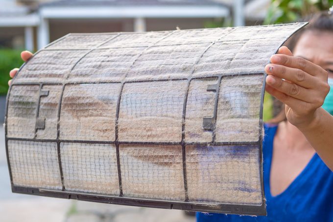 A Woman Holding A Dirty And Dusty Air Conditioner Filter to clean the filter
