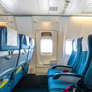 Comfortable Seats In Cabin Of Huge Aircraft With Screens In Chairs Back, emergency exit door and seat trays pictured in a bright cabin