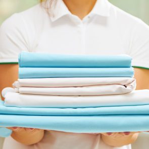 Closeup Of Woman's Hand Holding A Stack Of Clean Folded Bed Sheets Of Blue And White Colors