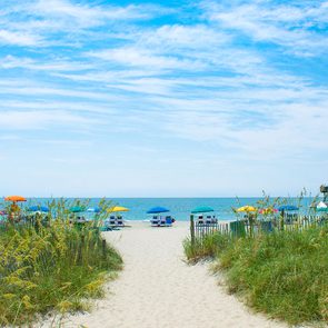 Footpath to the ocean with Beach chairs and parasols on the sand in the background