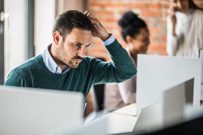 Young worried businessman working on laptop at corporate office.