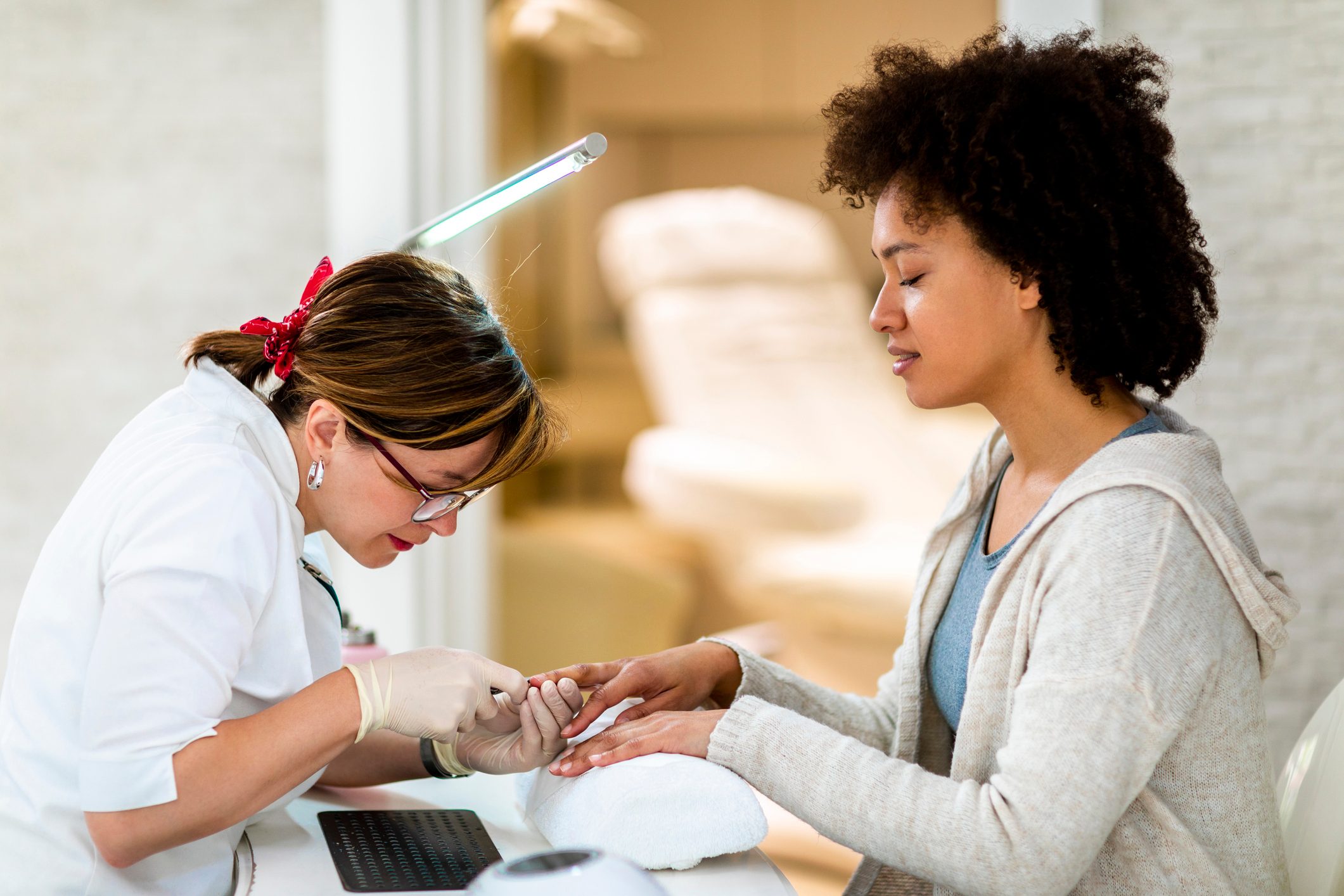 Female manicurist using a cuticle trimmer tool to tidy up a multi-ethnic woman's fingernail in a manicure salon