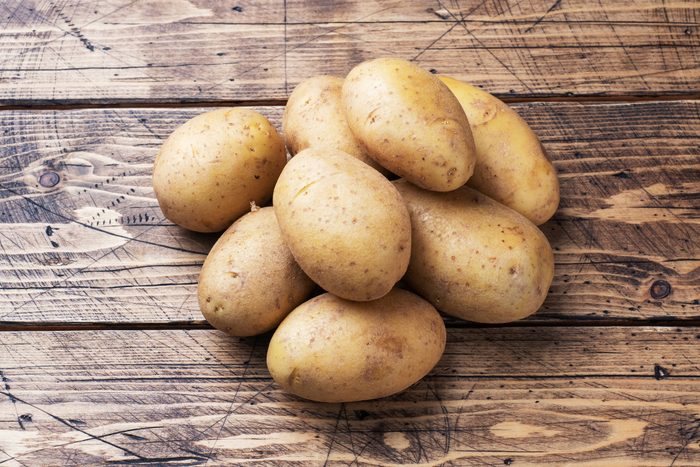 Several tubers of raw potatoes on a wooden background. Copy space.
