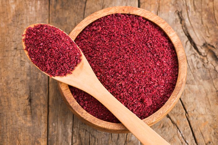 Dried ground red Sumac powder spices in wooden spoon and bowl on rustic table. Healthy food concept