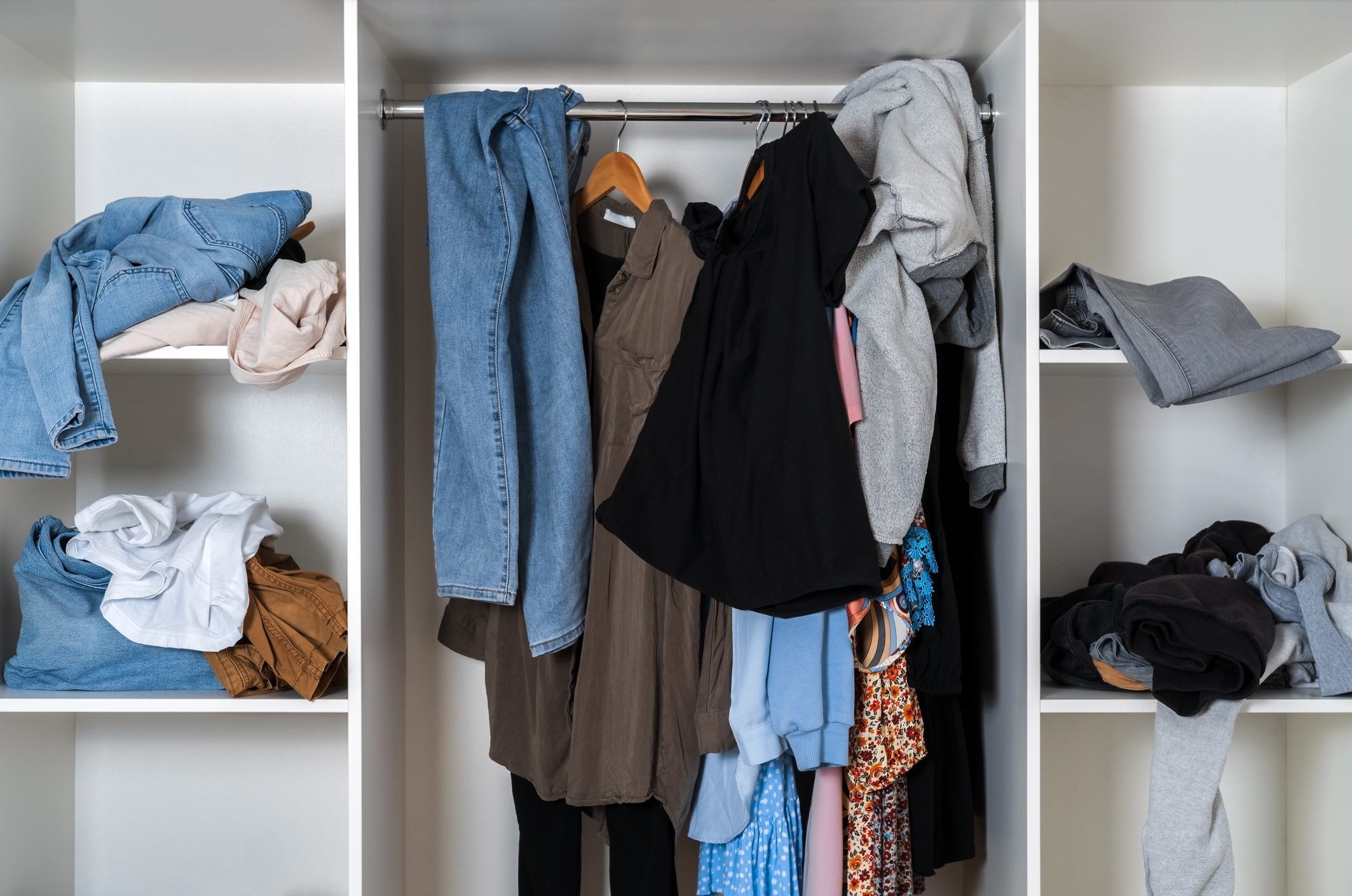 Messy dressing room shelves with stack of clothes.