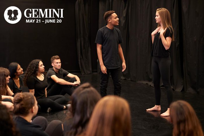 two people standing while a group of others sit on the ground around them during an improv class