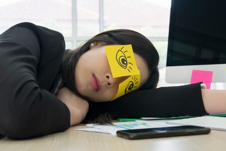 Close up young woman employee, drawing funny eyes drawing on her eyes and sleepy on the office desk.