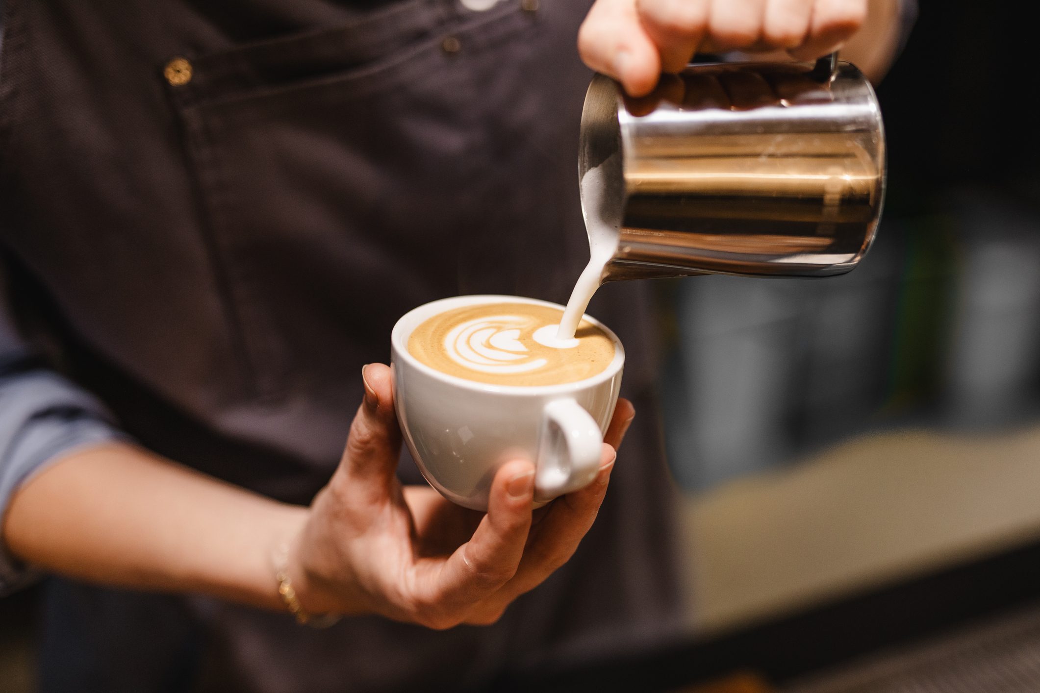 close up view of Young woman preparing a coffee by drawing a flower with milk