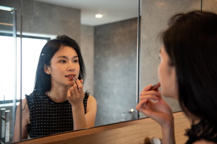Young businesswoman applying lipstick in front of the mirror