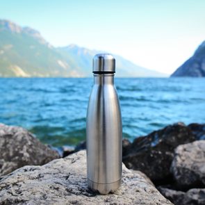 Steel eco thermo water bottle on the background of the lake in the mountains
