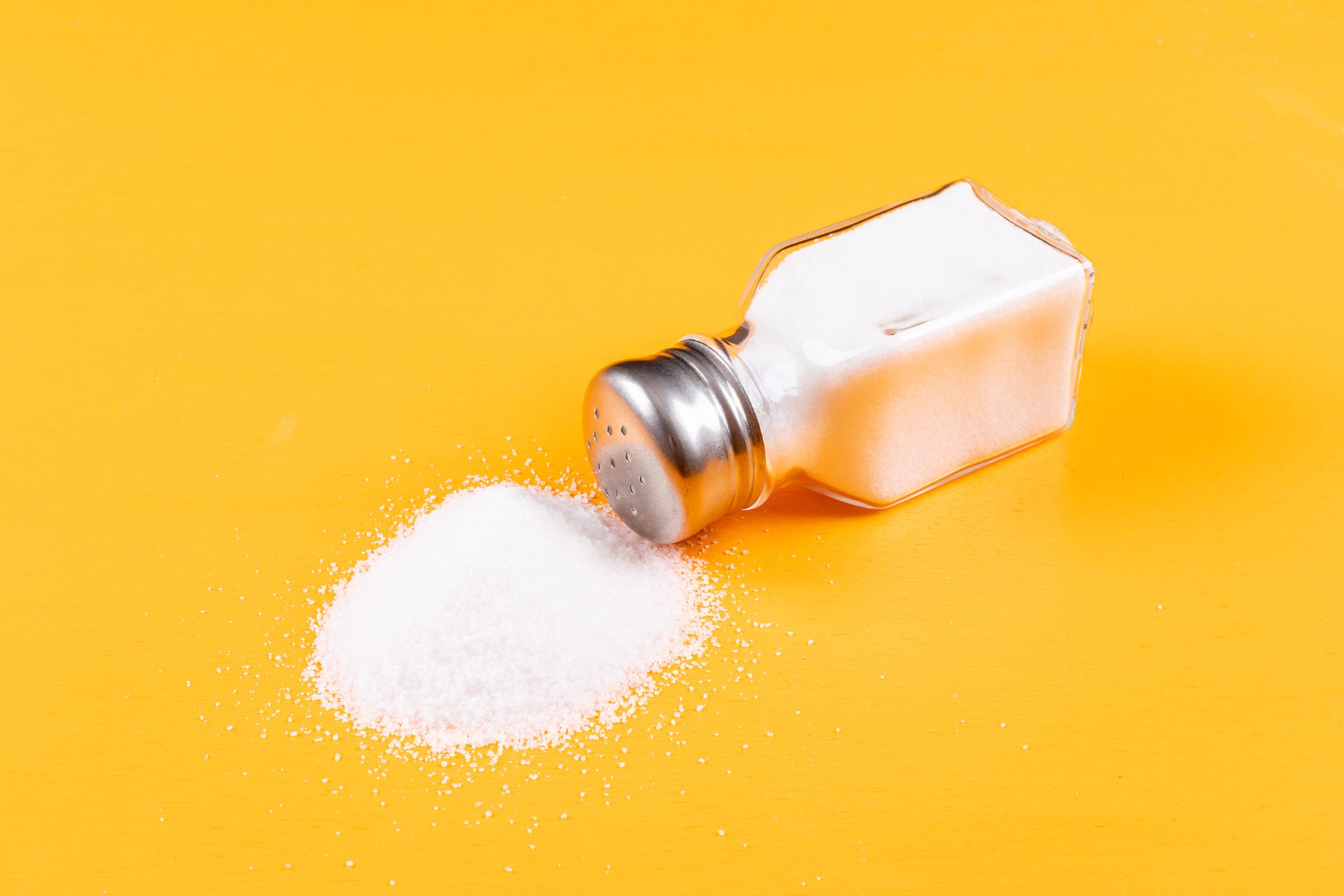 High angle view sea salt coming out of salt shaker on orange background horizontal,Romania