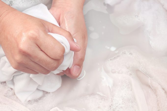Woman's hands washing white color clothes in the basin.