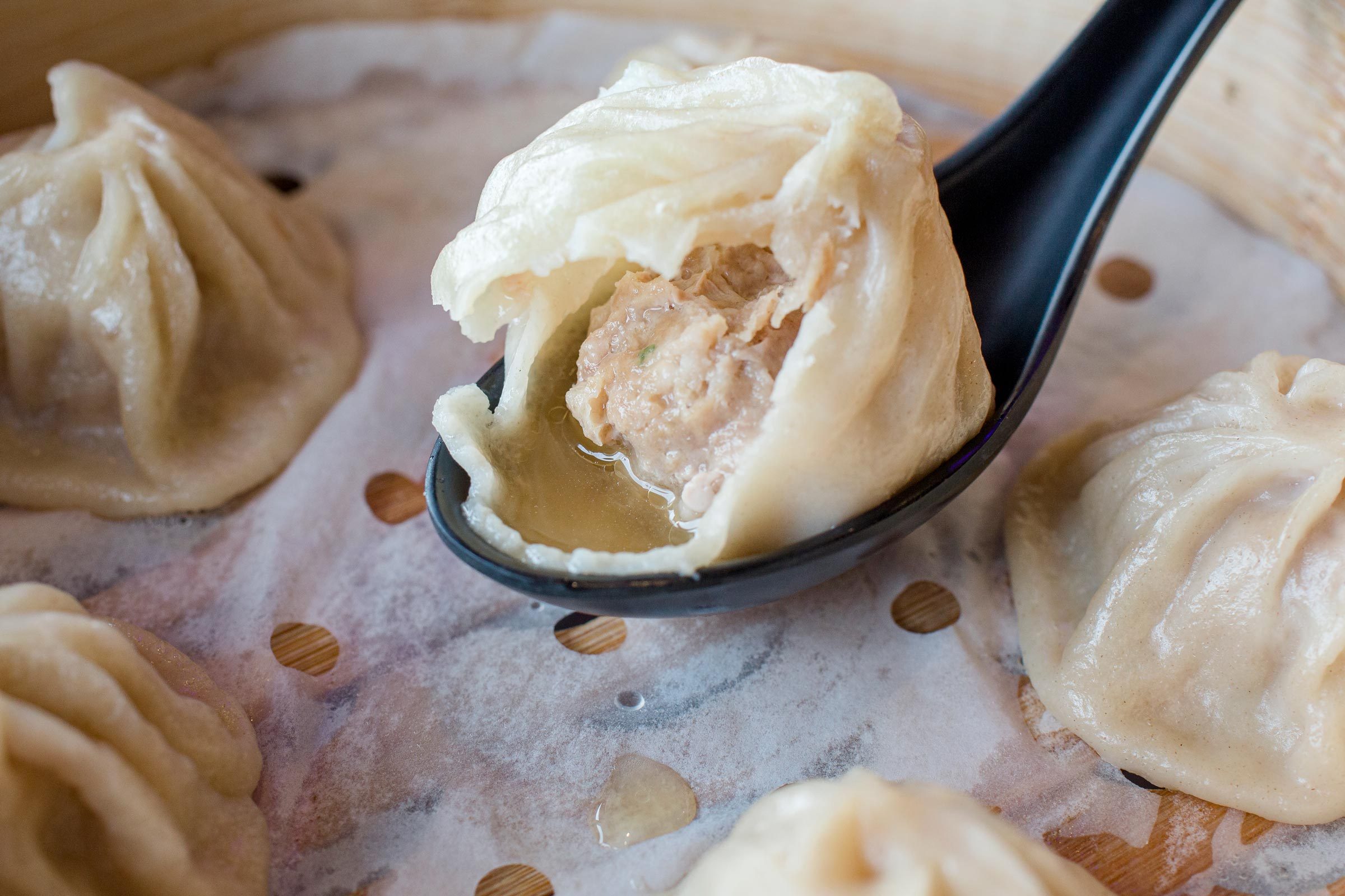 close-up of half-eaten soup dumpling resting on spoon in steam basket