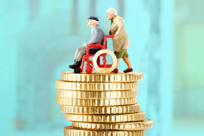 two elderly figurines on a stack of gold coins, turquoise background