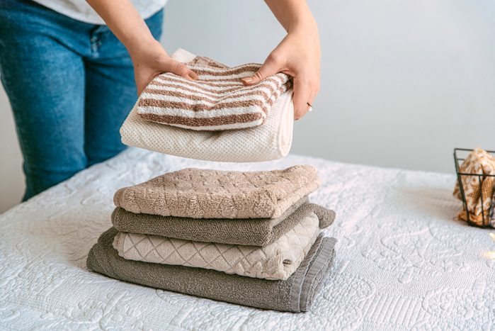 Woman folding stack of fresh laundry and towels, organizing laundry in boxes and baskets.