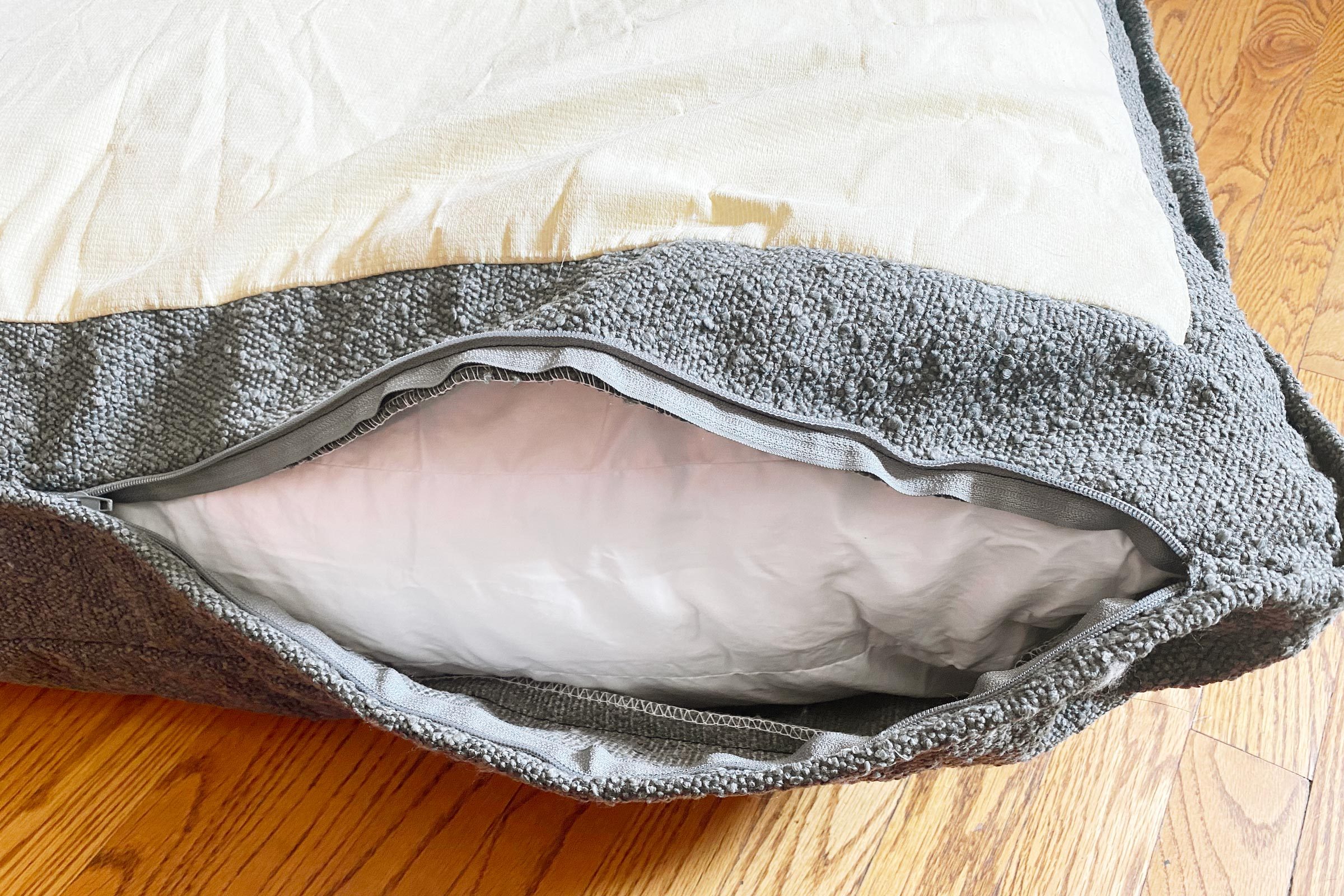 unzipped grey saatva dog bed on a wooden floor