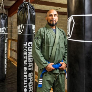 Mark Anthony Gonzales wearing a Brazilian Jiu Jitsu Gi, standing in front of sandbags.