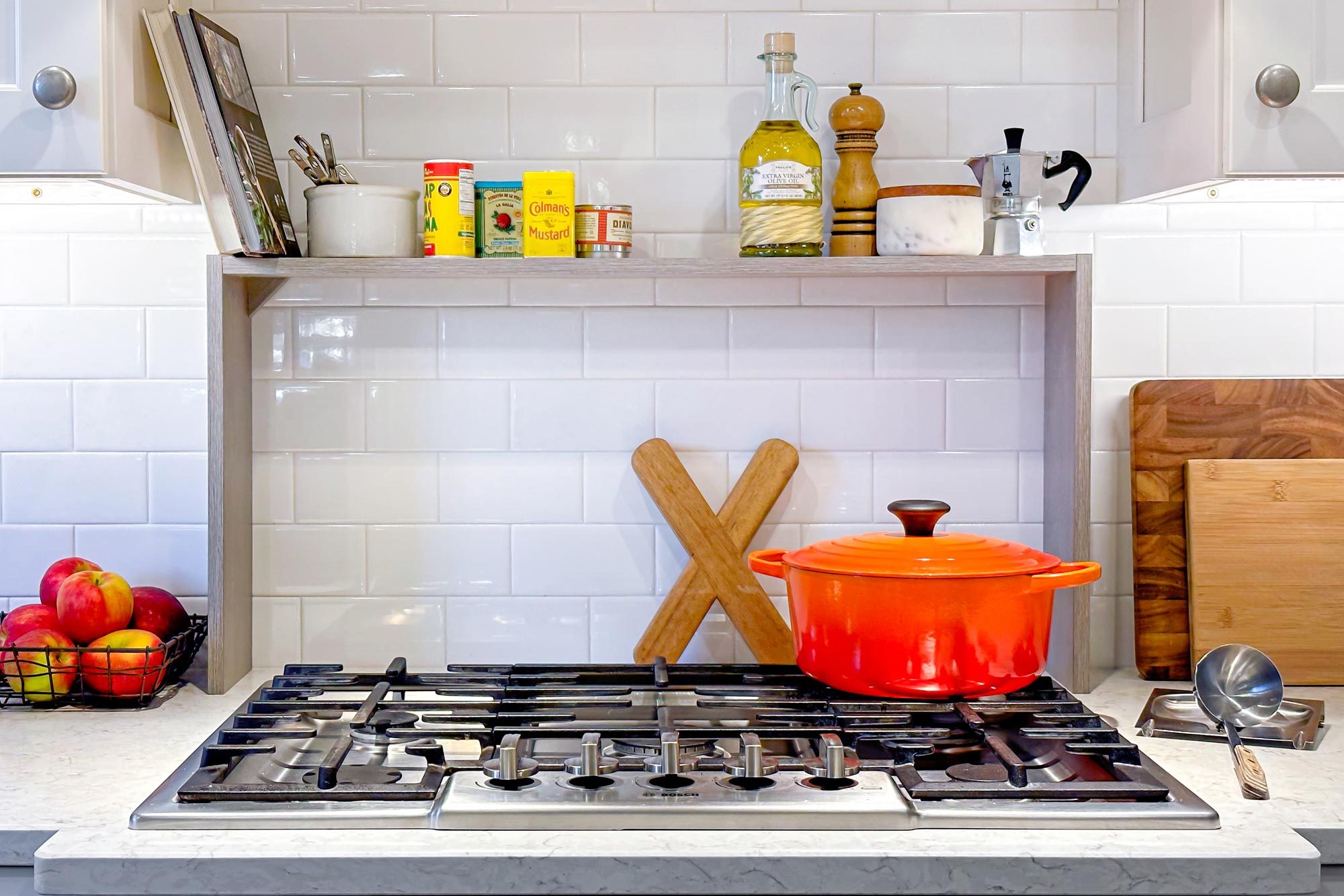 shelf over a stove in a kitchen with an orange dutch oven on the stove top