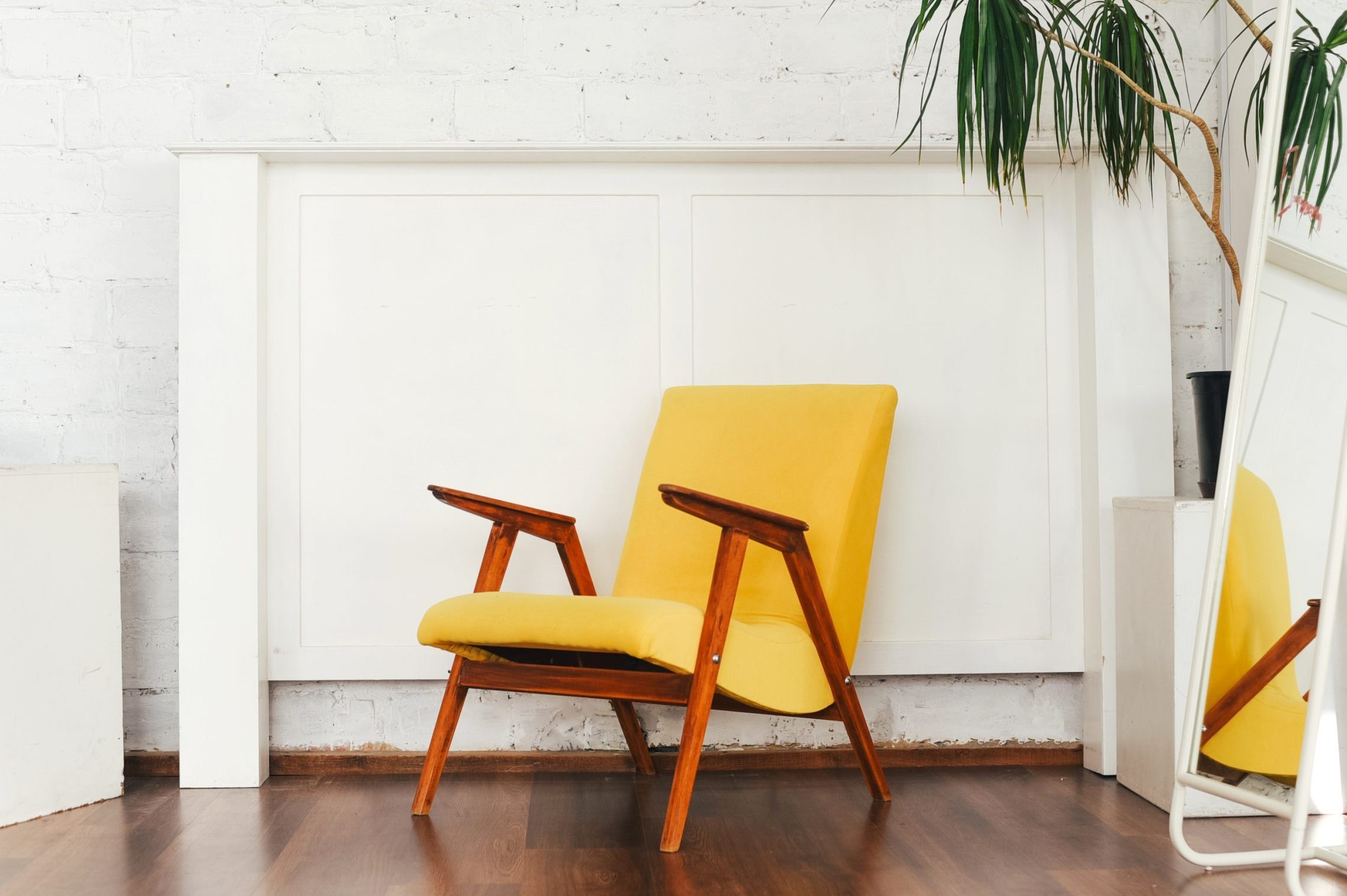 Yellow armchair and indoor flower against a white brick wall. Landscaping. Room decor. Light interior. Simplicity. Brick wall. Green palm. Home decor. Mirror.