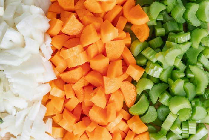 Overhead view of chopped courgette, onion, carrot and celery on a wooden chopping board