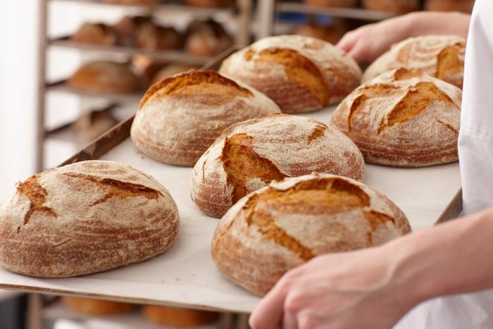 Chef Carrying Tray Of Bread In Industrial Bakery Kitchen