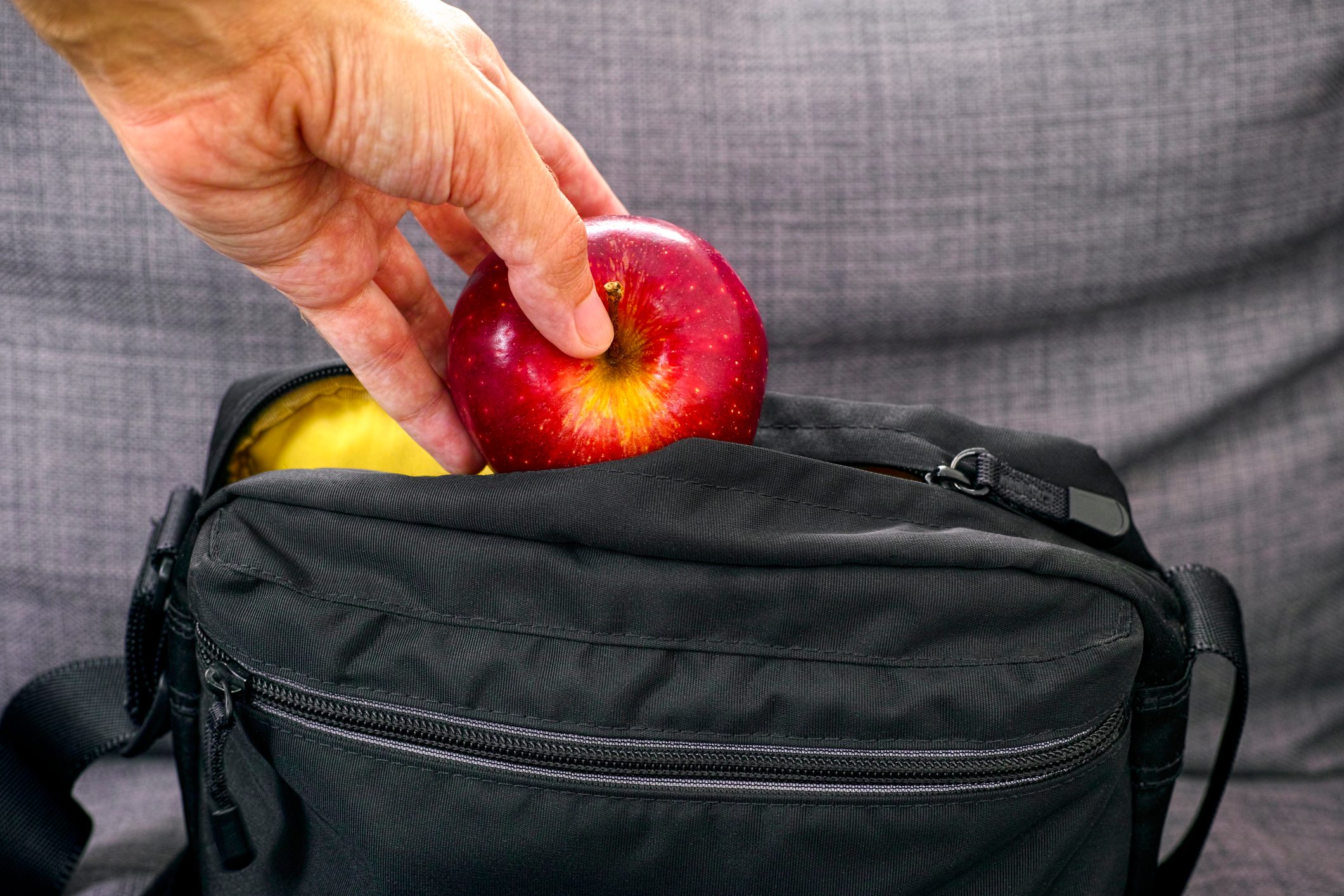 Person hand taking red apple from black bag.