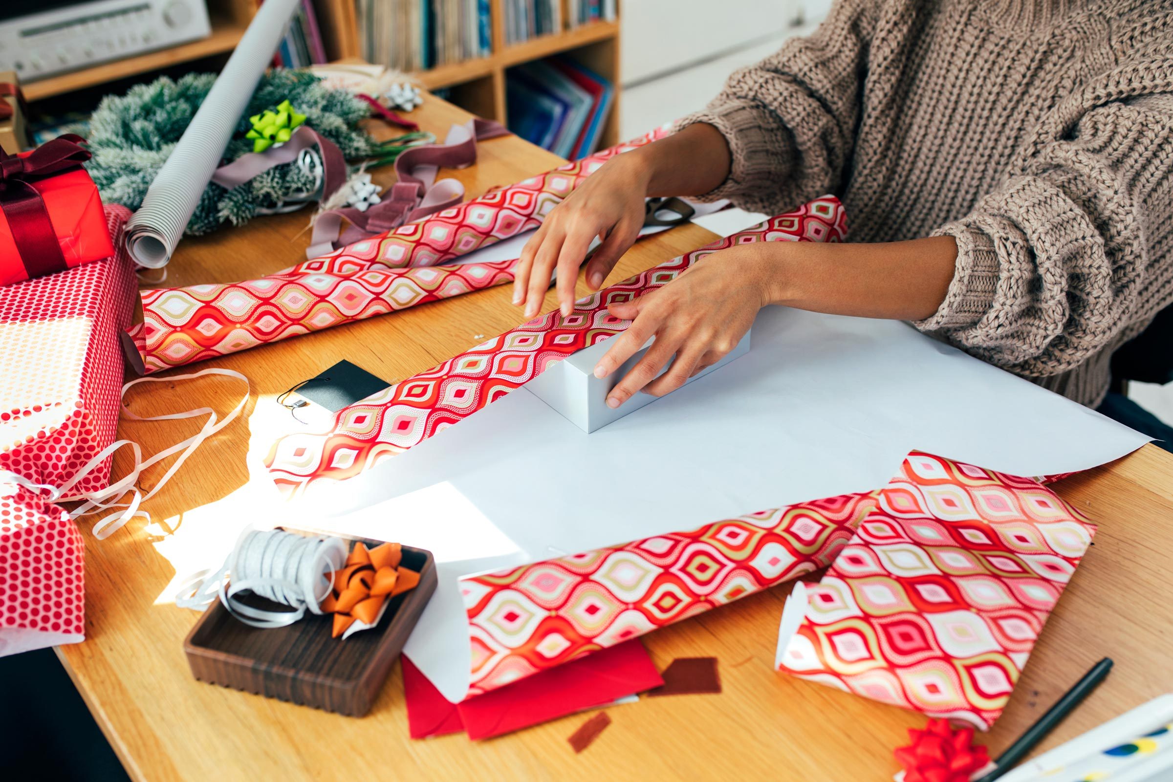 a young woman dressed in a cozy jumper wrapping Christmas presents at home.