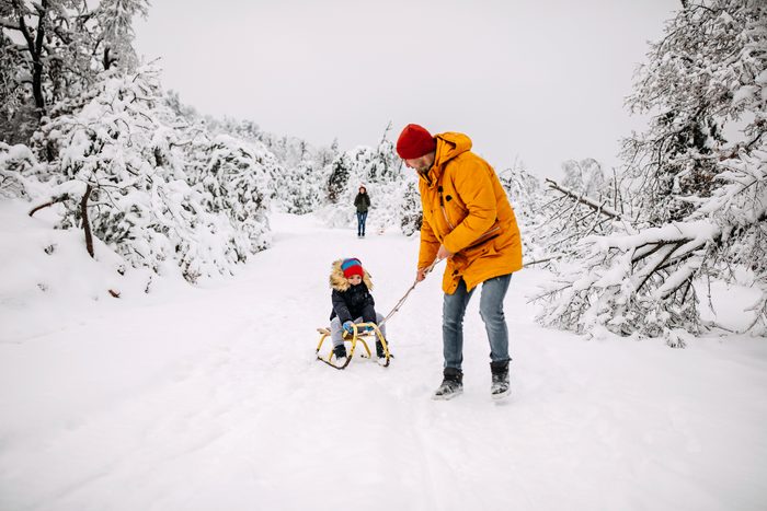 Father and son sledding in park on snowy winter day