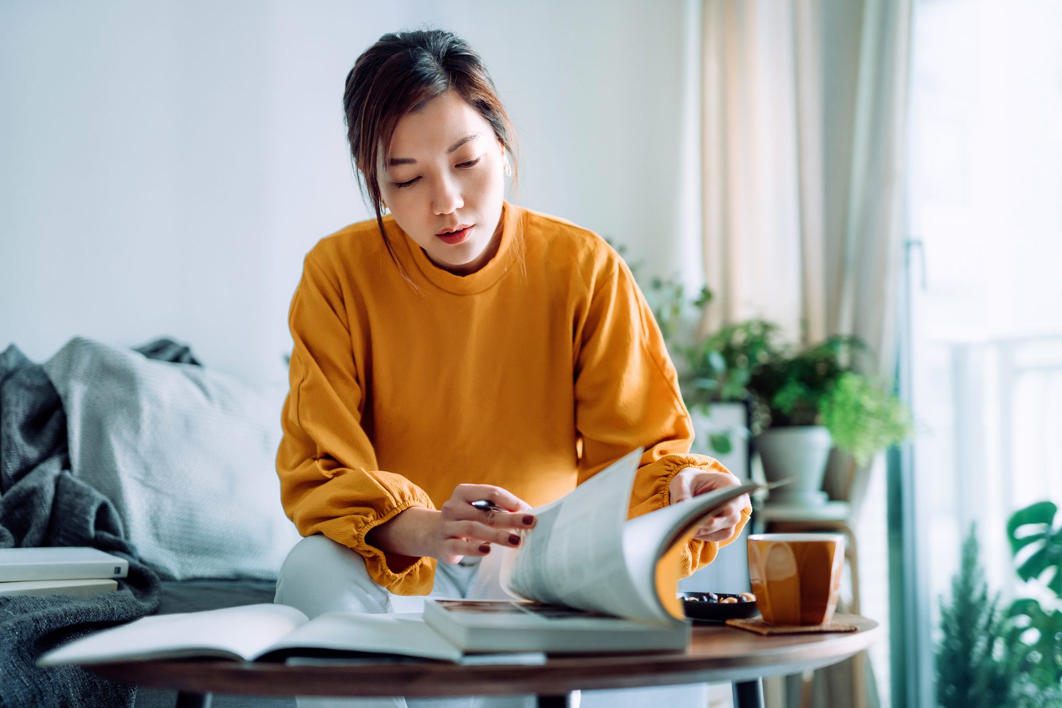 Focused young Asian woman reading books and making notes at home, concentrates on her studies. Further education concept