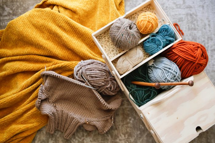 Wooden box with needlework, box with balls of yarn, wooden knitting needles and untied children's sweater.