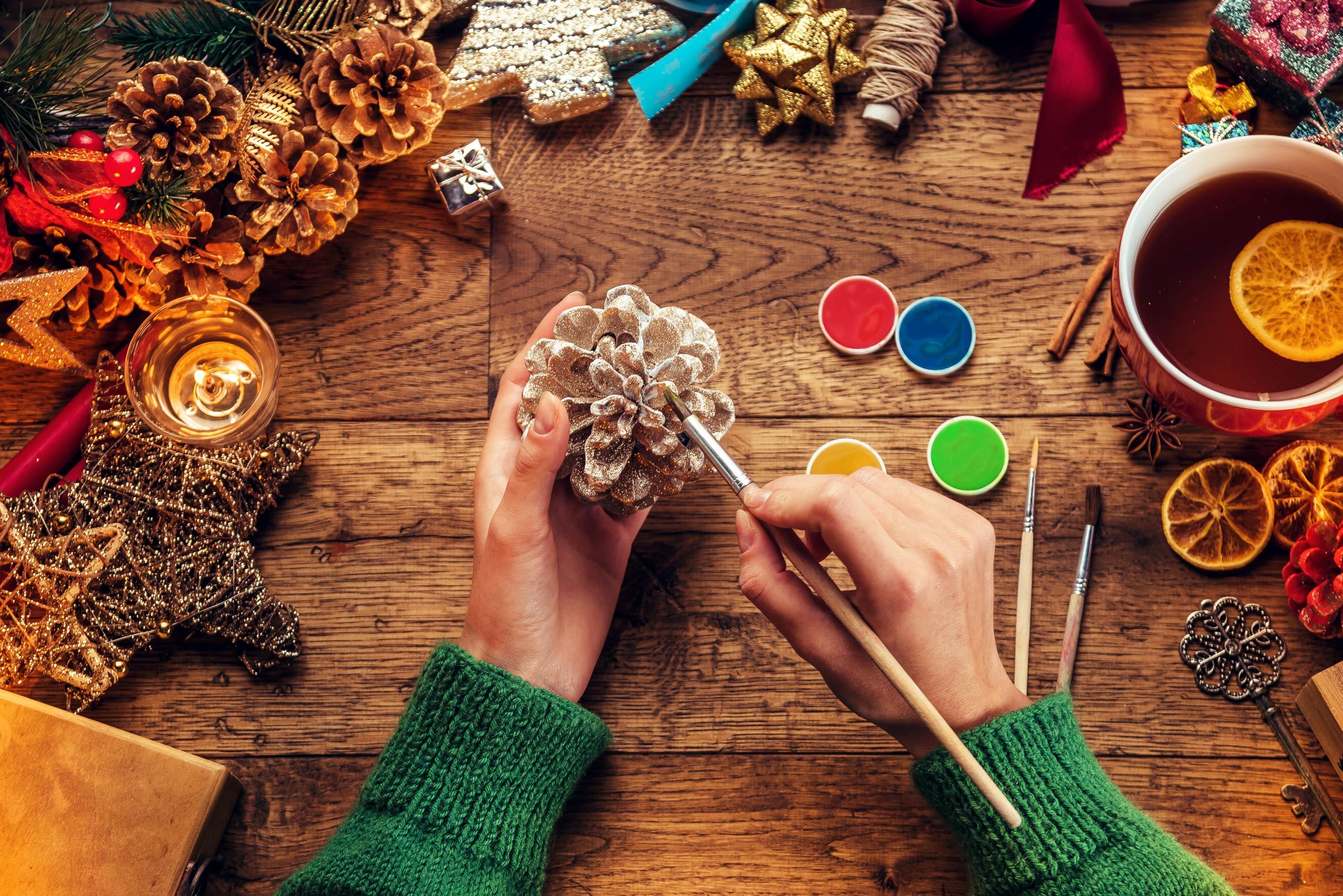 Woman painting small pine cone. Christmas time.