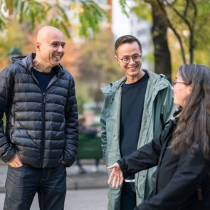 One woman and two men walking and talking together on street