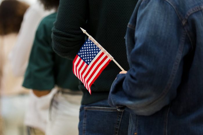 Diverse group in line to vote; one holds American flag
