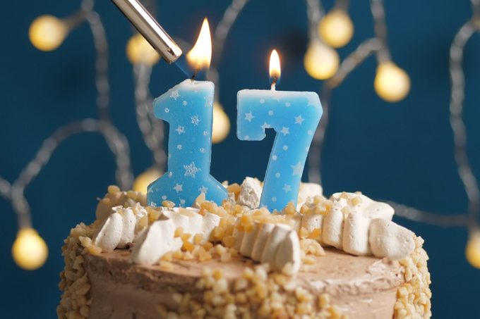 Birthday cake with 17 number candle on blue backgraund set on fire by lighter. Close-up