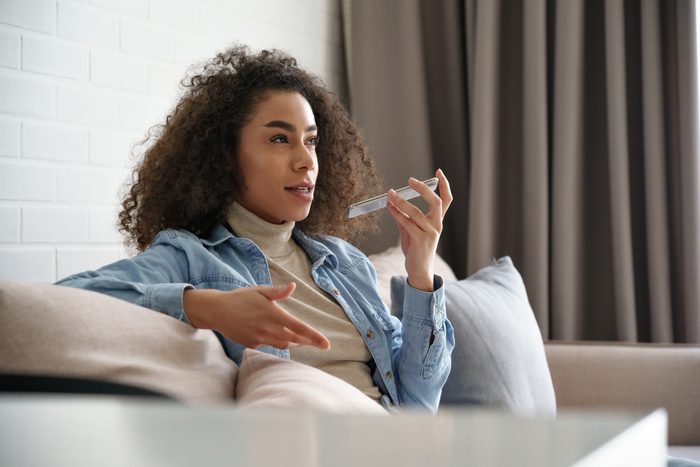 African girl holding phone speak on speakerphone, using virtual digital voice recognition assistant search, record audio message on smartphone at home. Mobile app ai digital tech assistance concept