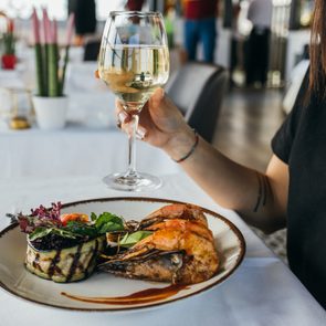 Woman eating grilled scampi with white wine at restaurant