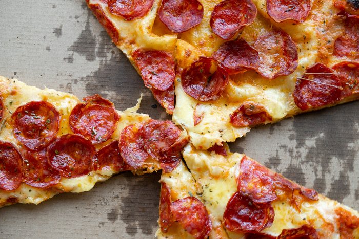 Delicious Italian pizza in a pizza box and a delivery box, on the table in a pizzeria. Sliced pizza slice with tomatoes, pepperoni sausage and cheese. The concept of unhealthy lifestyle, overeating, junk food, fast food. Delivery to your home or work.