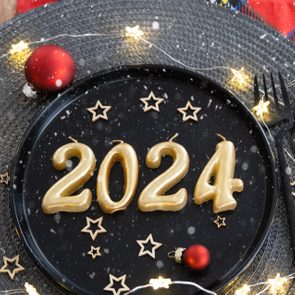 Golden figures 2024 from candles on a black plate on a festive table with a New Year's serving. Loft-style interior, party, feast. Wicker napkin, fork, knife
