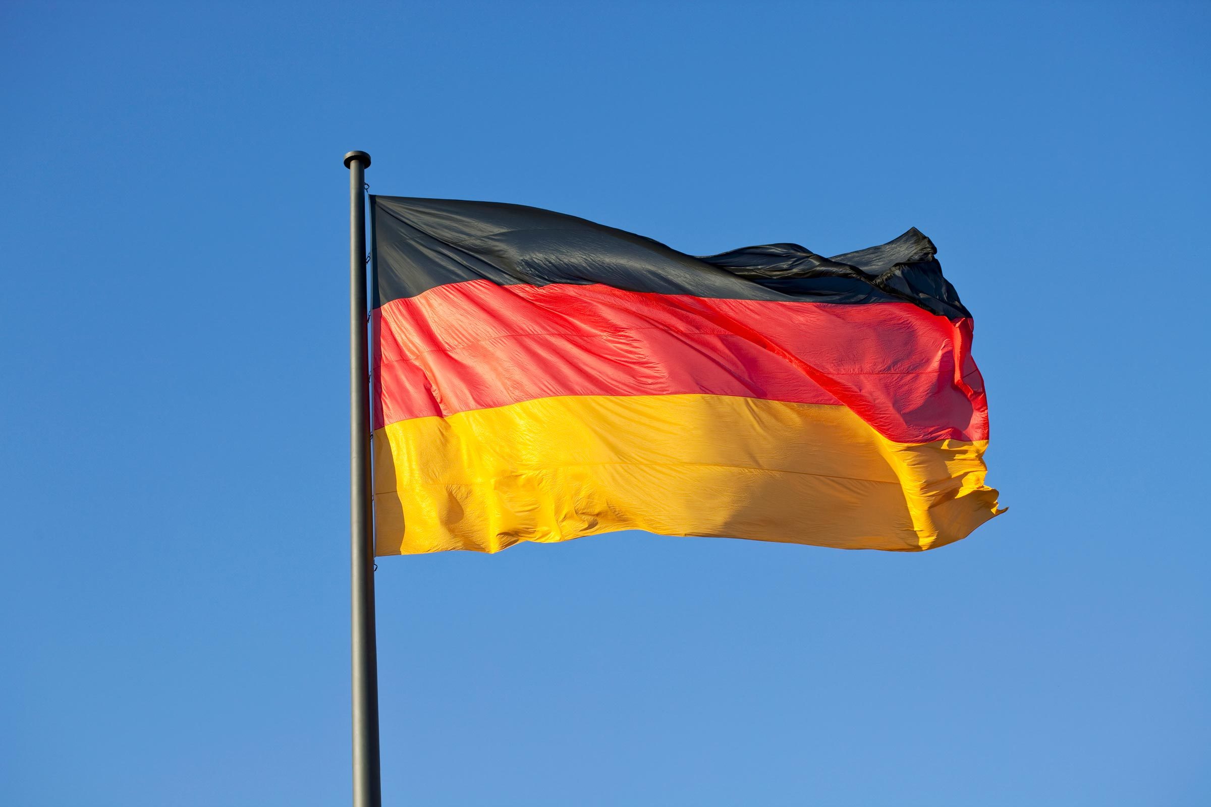 A German flag on a flag pole with blue sky