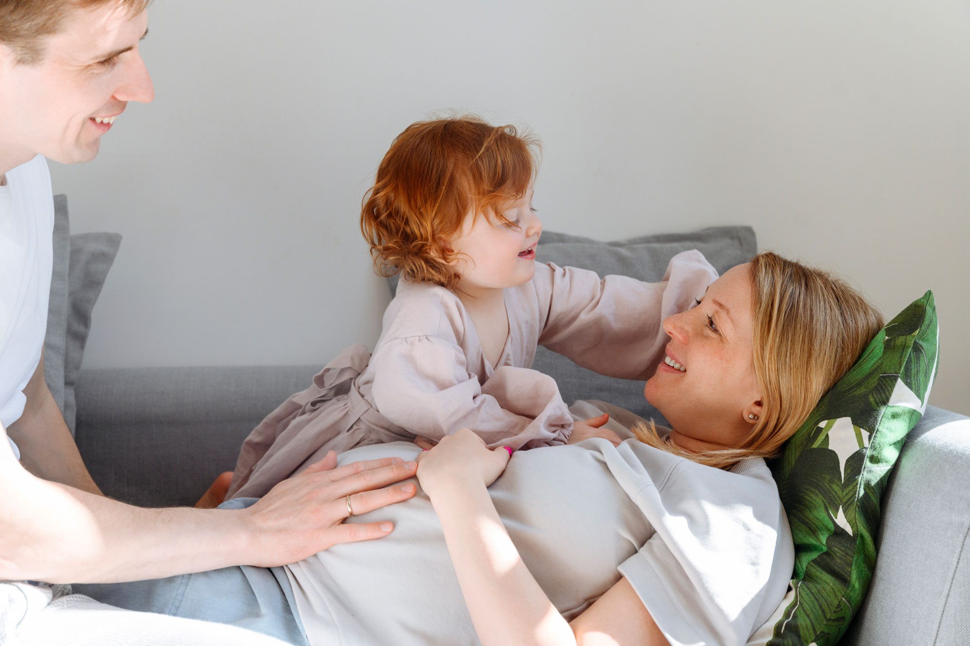 Cute Daughter Admiring Pregnant Mother By Father On Sofa At Home