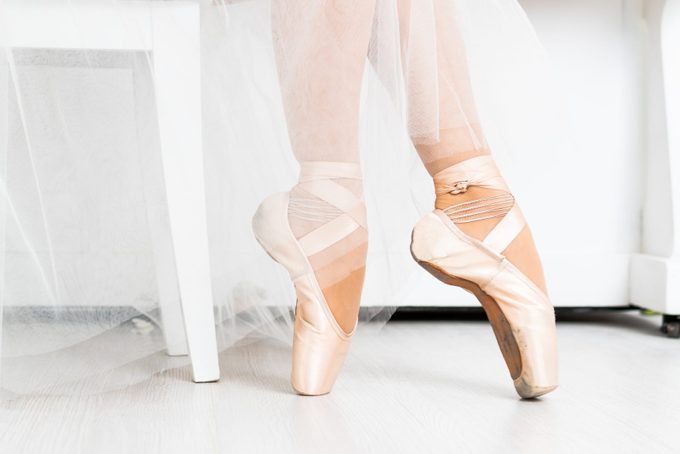 Close-up of dancing legs of ballerina wearing white pointe on a white background