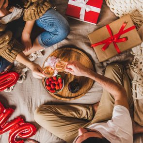 Young couple sitting in bed, giving presents drinking rose champagne