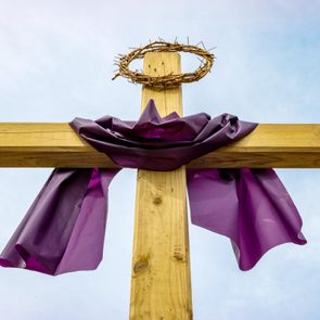 Wooden cross with crown of thorns and purple Lent cloth outside on sunny day