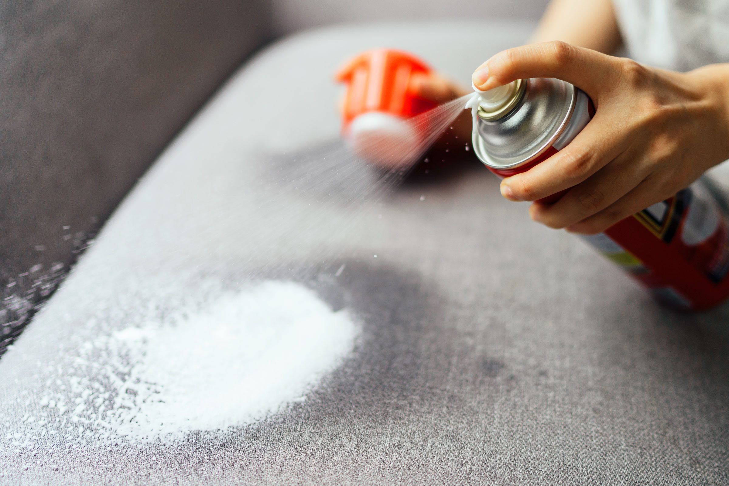 spraying cleaner onto a grey couch to clean dog pee