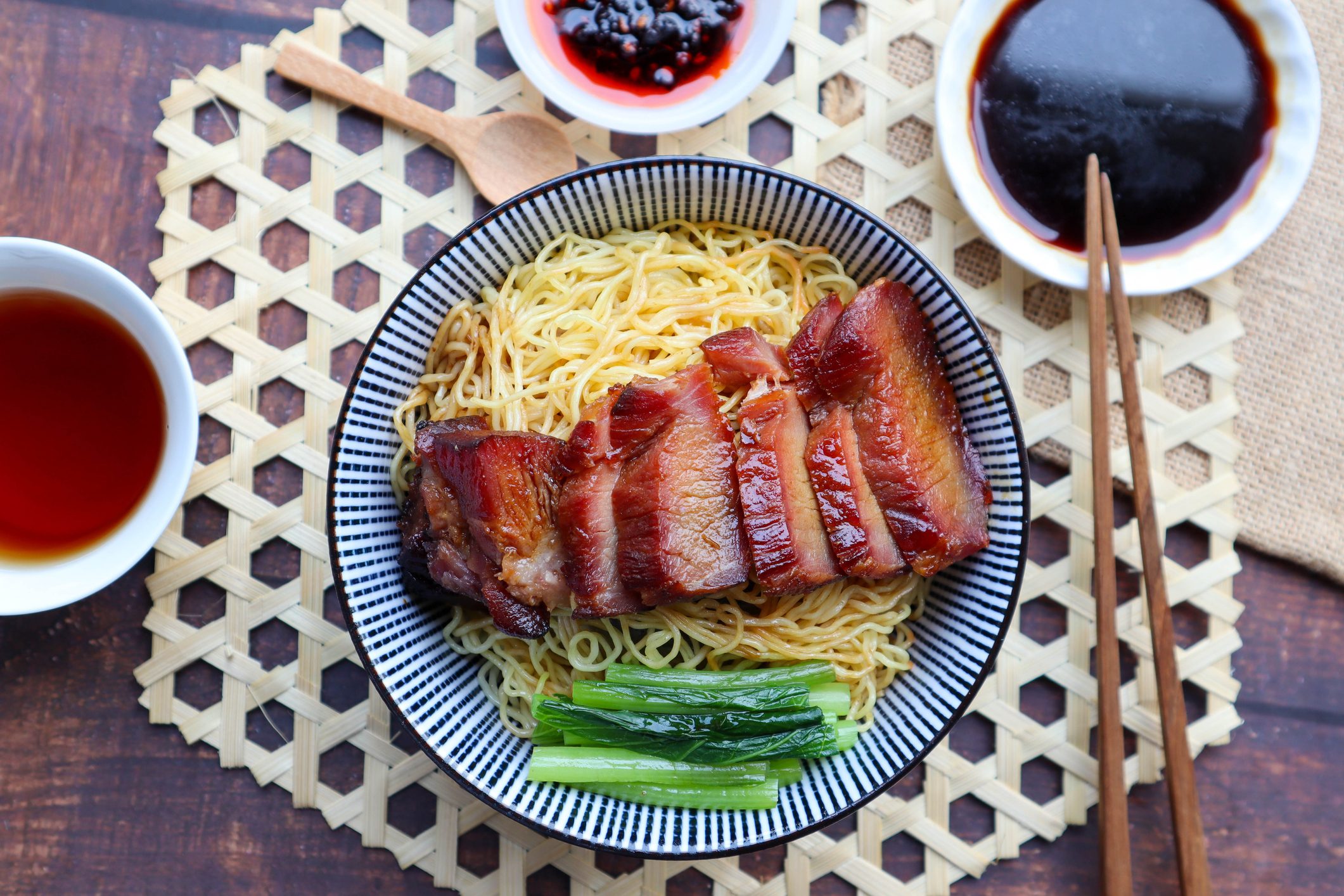 Chinese barbecue roast pork noodle (Char Siu) in a bowl on bamboo placemat of wood table - Top view Asian food