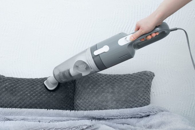 Handheld vacuum cleaner in hand. Vacuums fur decorative pillows on bed.
