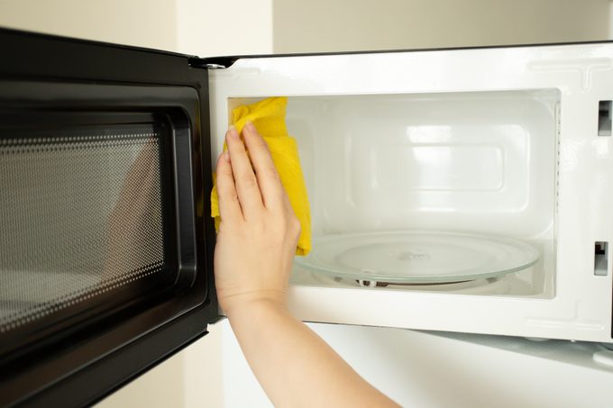 a woman's hand washes a microwave with a rag, cleanliness and hygiene in the kitchen