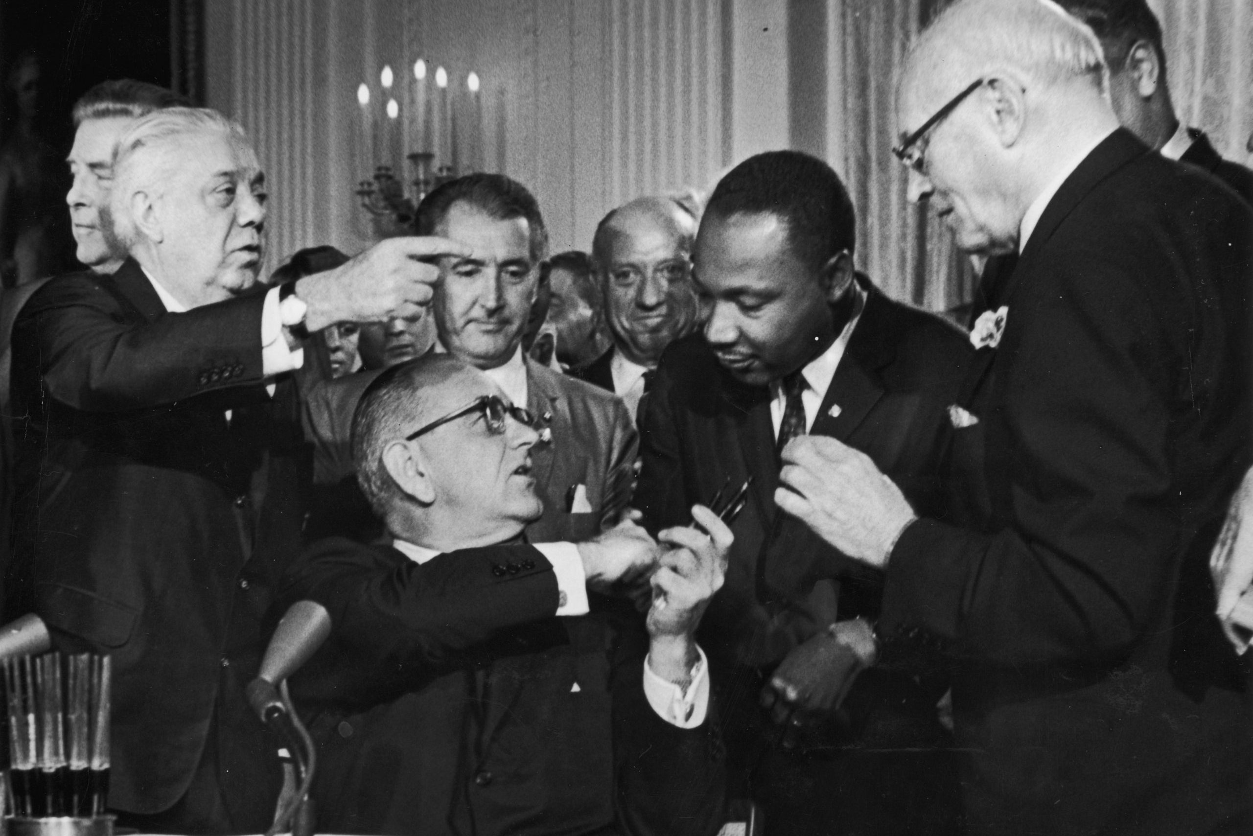 US President Lyndon B Johnson shakes the hand of Dr Martin Luther King Jr (1929 - 1968) at the signing of the Civil Rights Act while officials look on, Washington DC. (Photo by Hulton Archive/Getty Images)